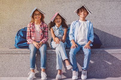 Drei fröhliche Schulkinder sitzend auf Stufe mit Schulbüchern auf dem Kopf