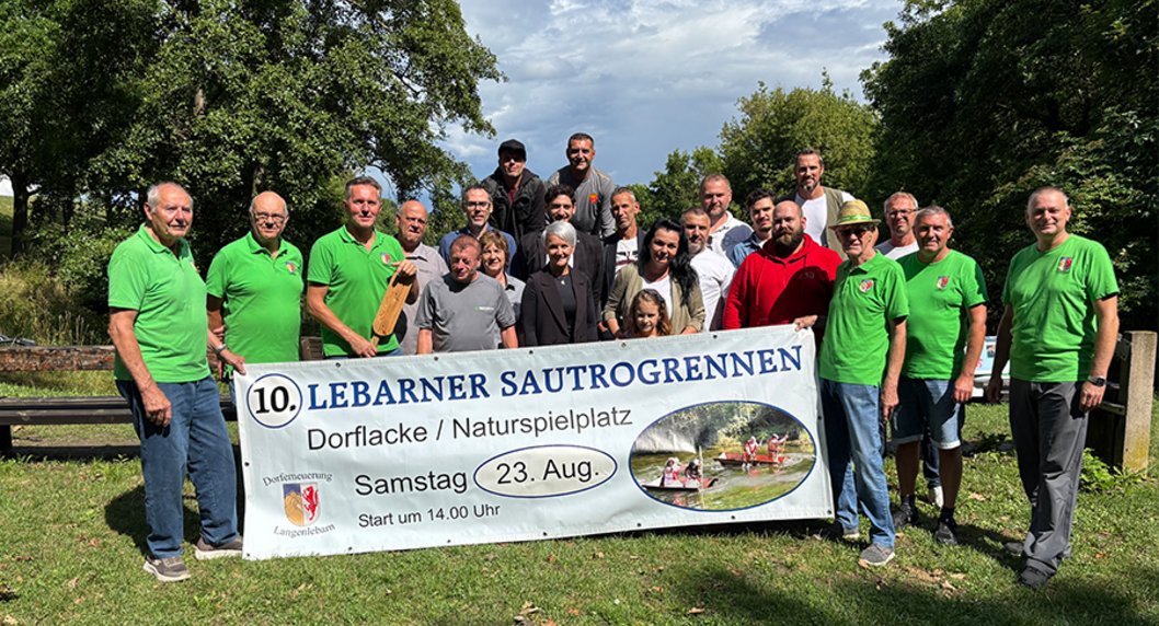Ankündigung Lebarner Sautrogrennen Männer mit grünem T-Shirt halten einen Banner