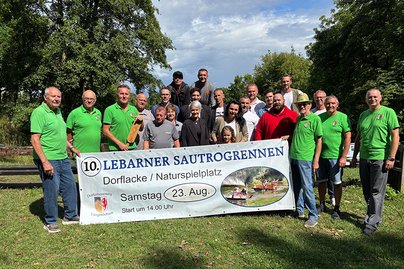 Ankündigung Lebarner Sautrogrennen Männer mit grünem T-Shirt halten einen Banner