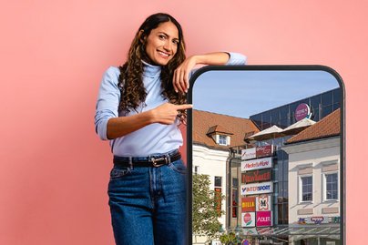 lachsfarbener Hintergrund mit Frau in Jeans die an einem überdimensionalen Handy lehnt