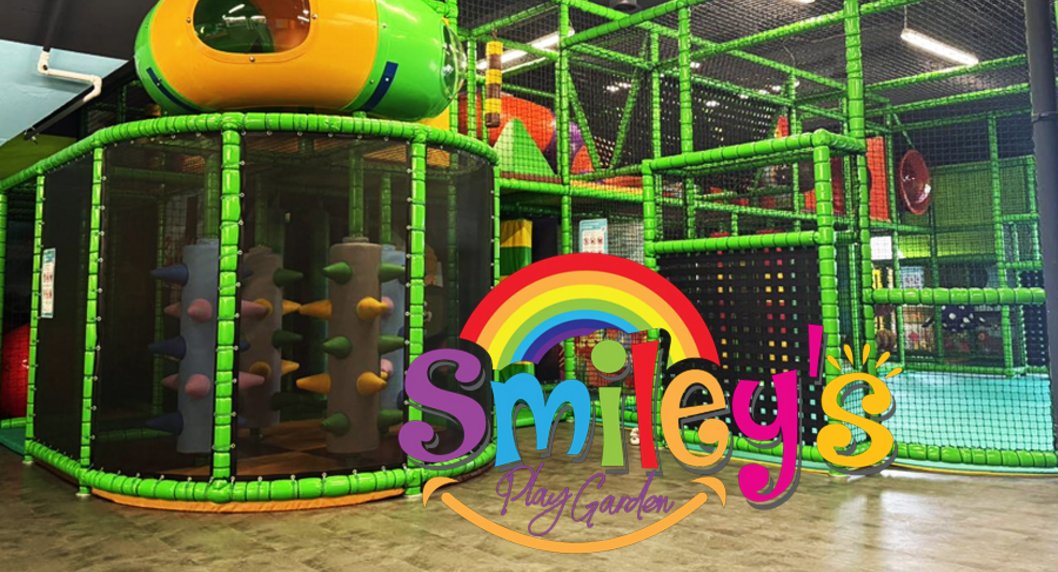 buntes Logo von Smileys Play Garden im Hintergrund das grüner Klettergerüst