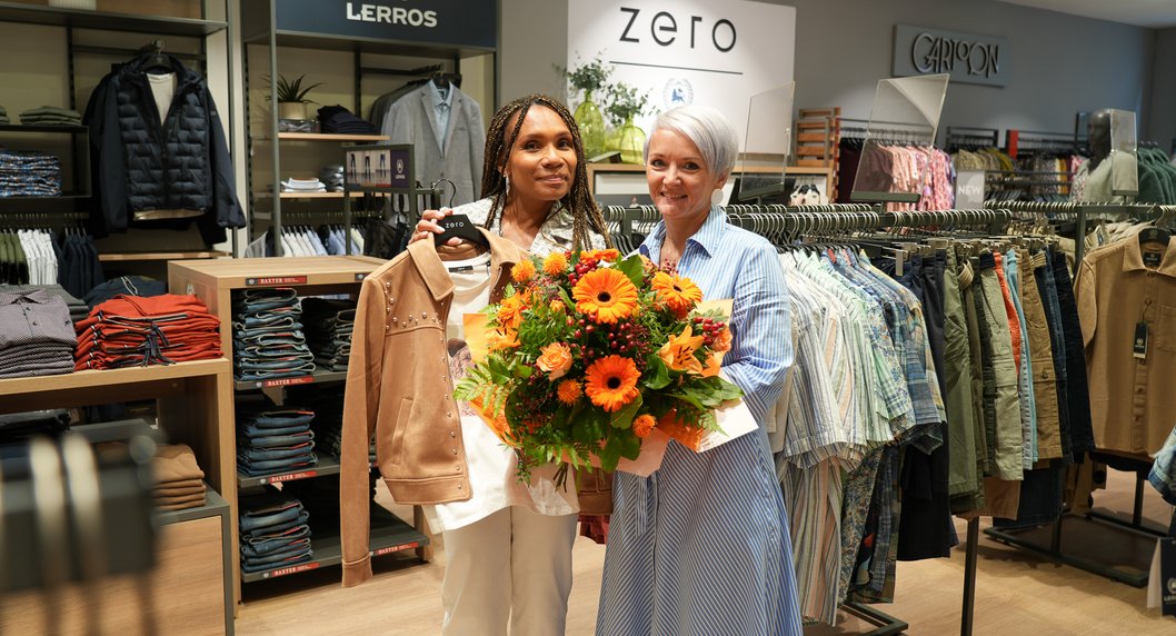 Sabine Riederer mit Blumenstrauß in der Hand und Mitarbeiterin von ZERO-Lerros bei Wiedereröffnung